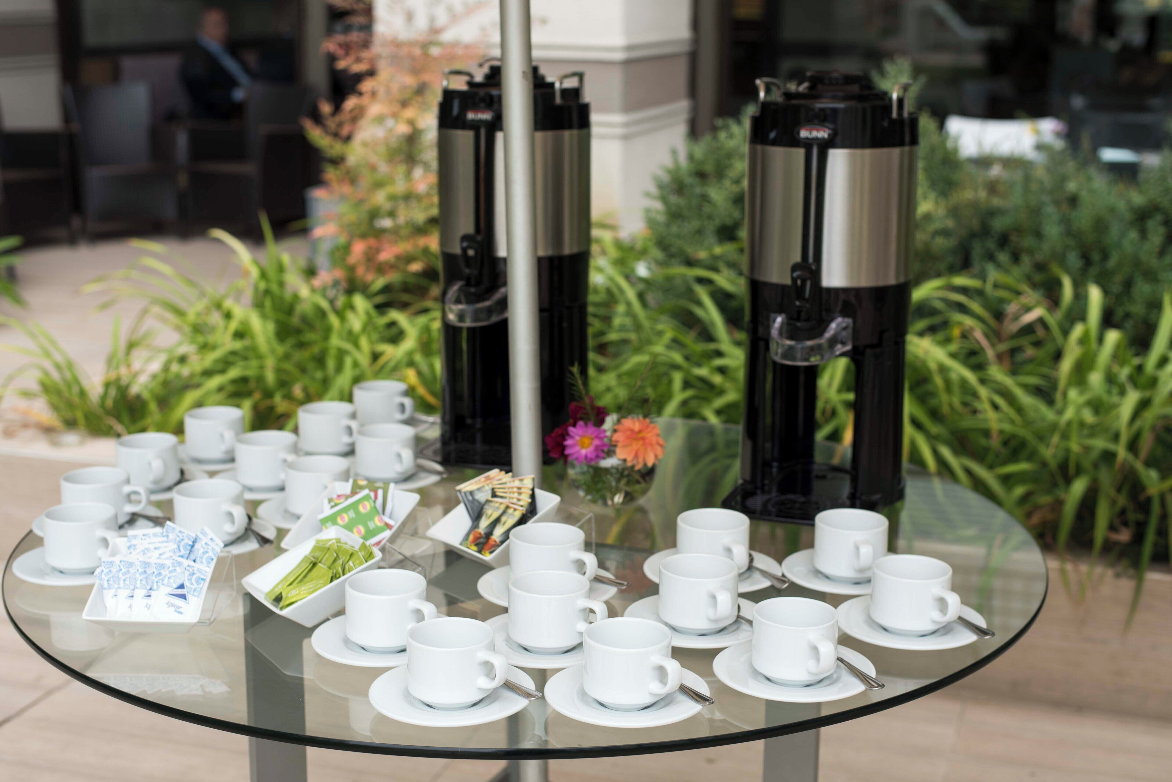 A glass table with white cups and saucers, a coffee maker, and a menu.