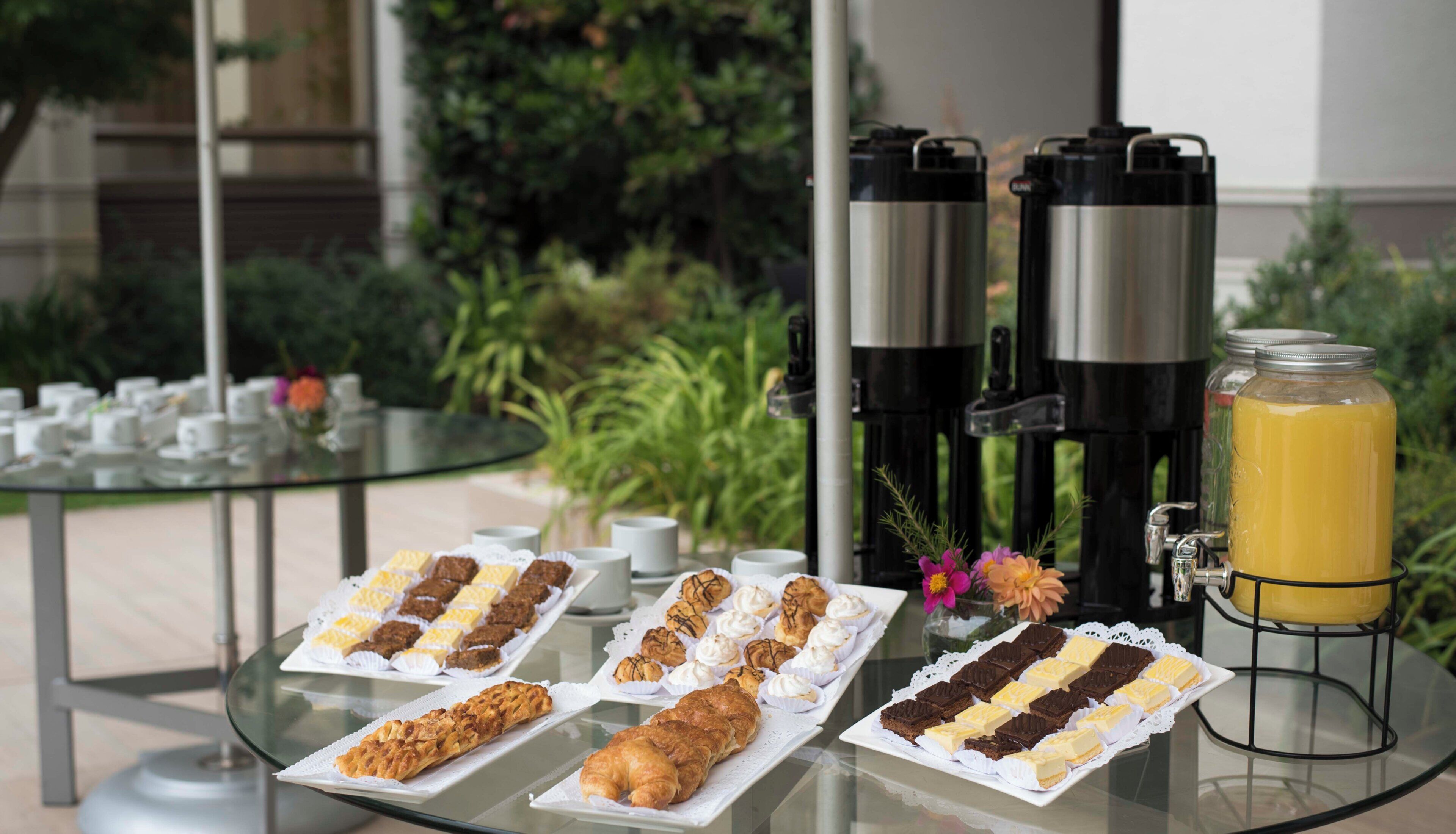 Una mesa de buffet con pasteles, una estación de café y un dispensador de zumo.