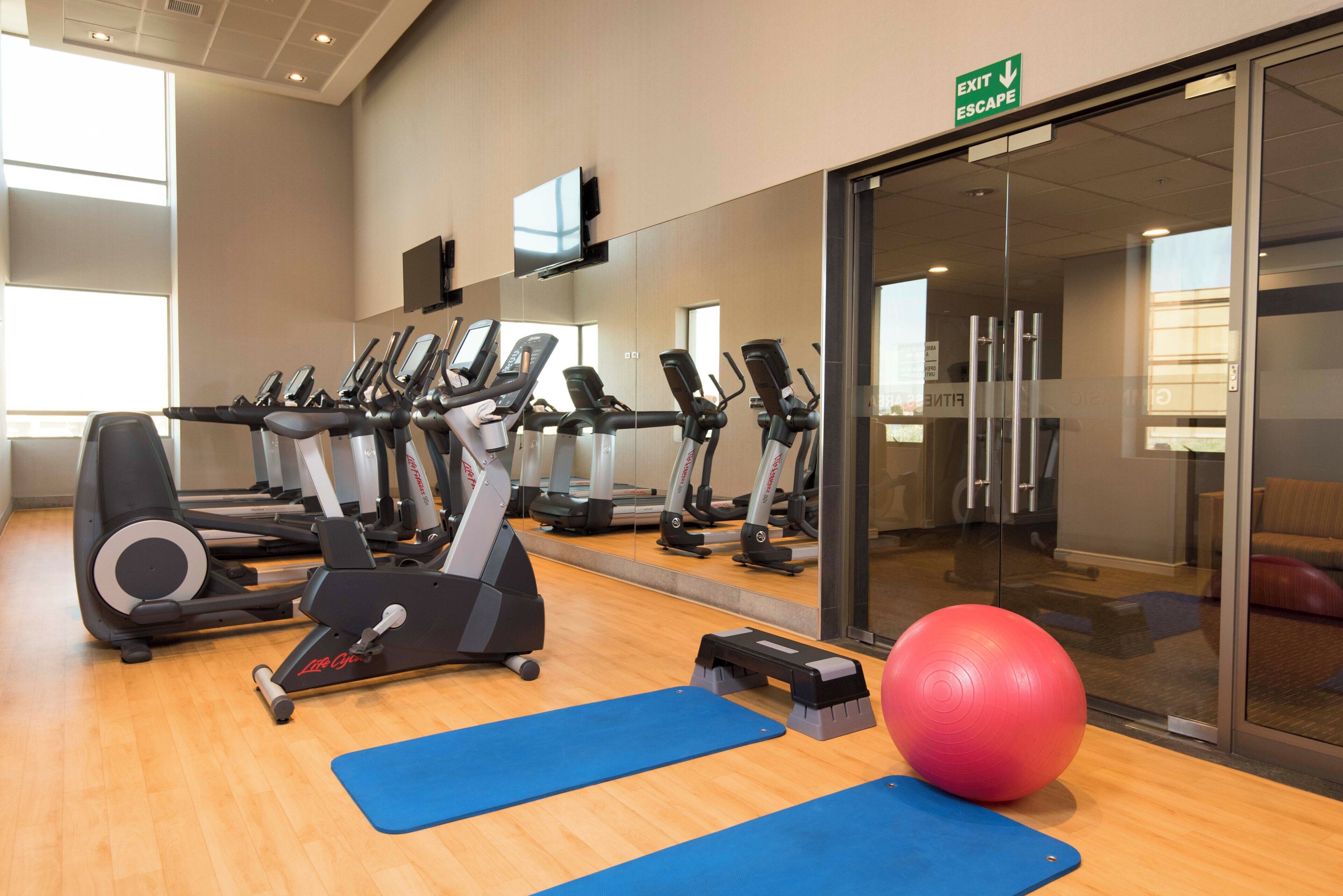 Une salle de sport équipée de plusieurs appareils d’exercice, d’un grand miroir et de tapis de sol.