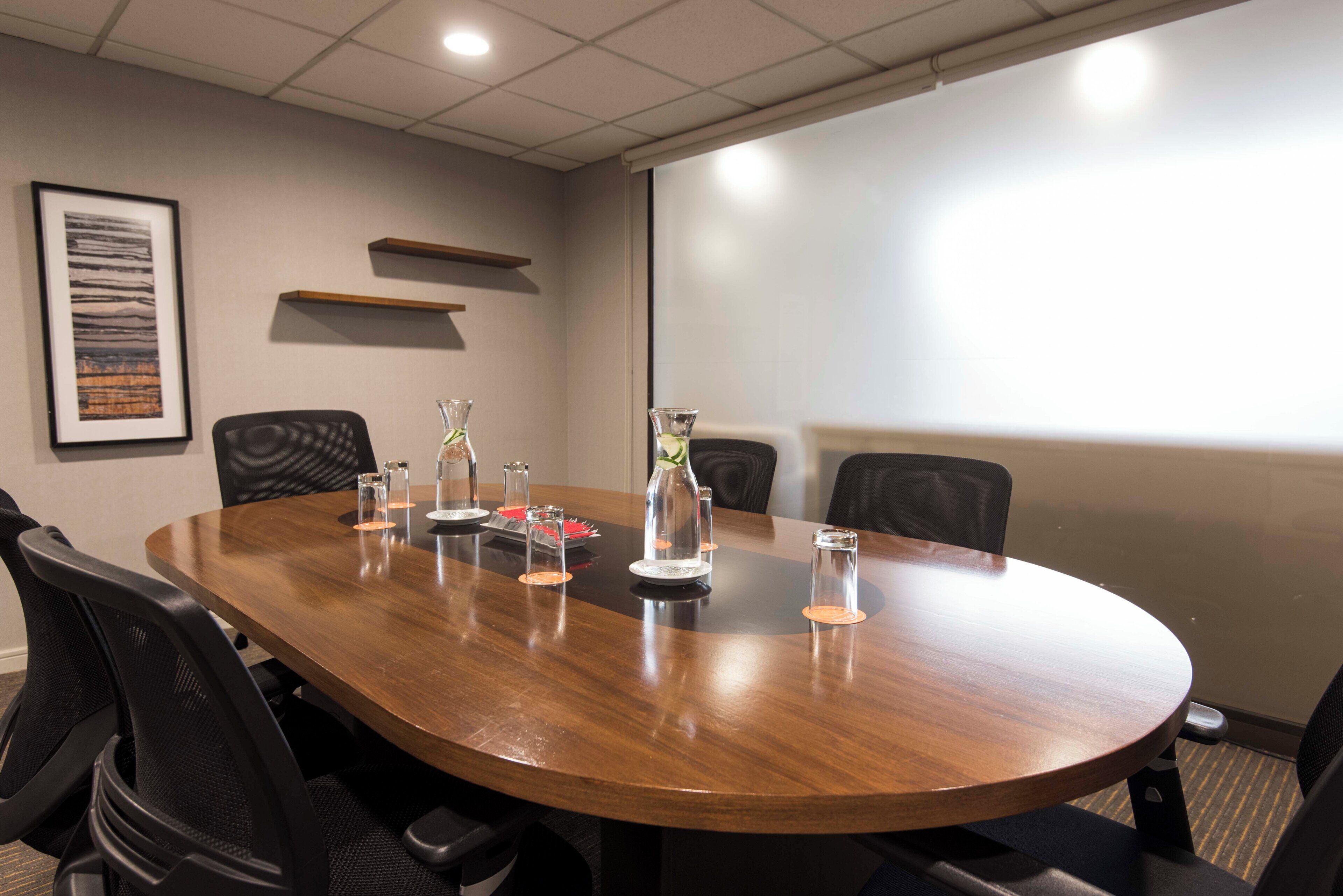 A conference room with a wooden table, chairs, and a projector screen.