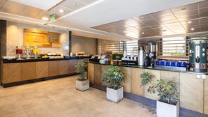 A modern kitchen with a long counter, coffee machines, and potted plants.
