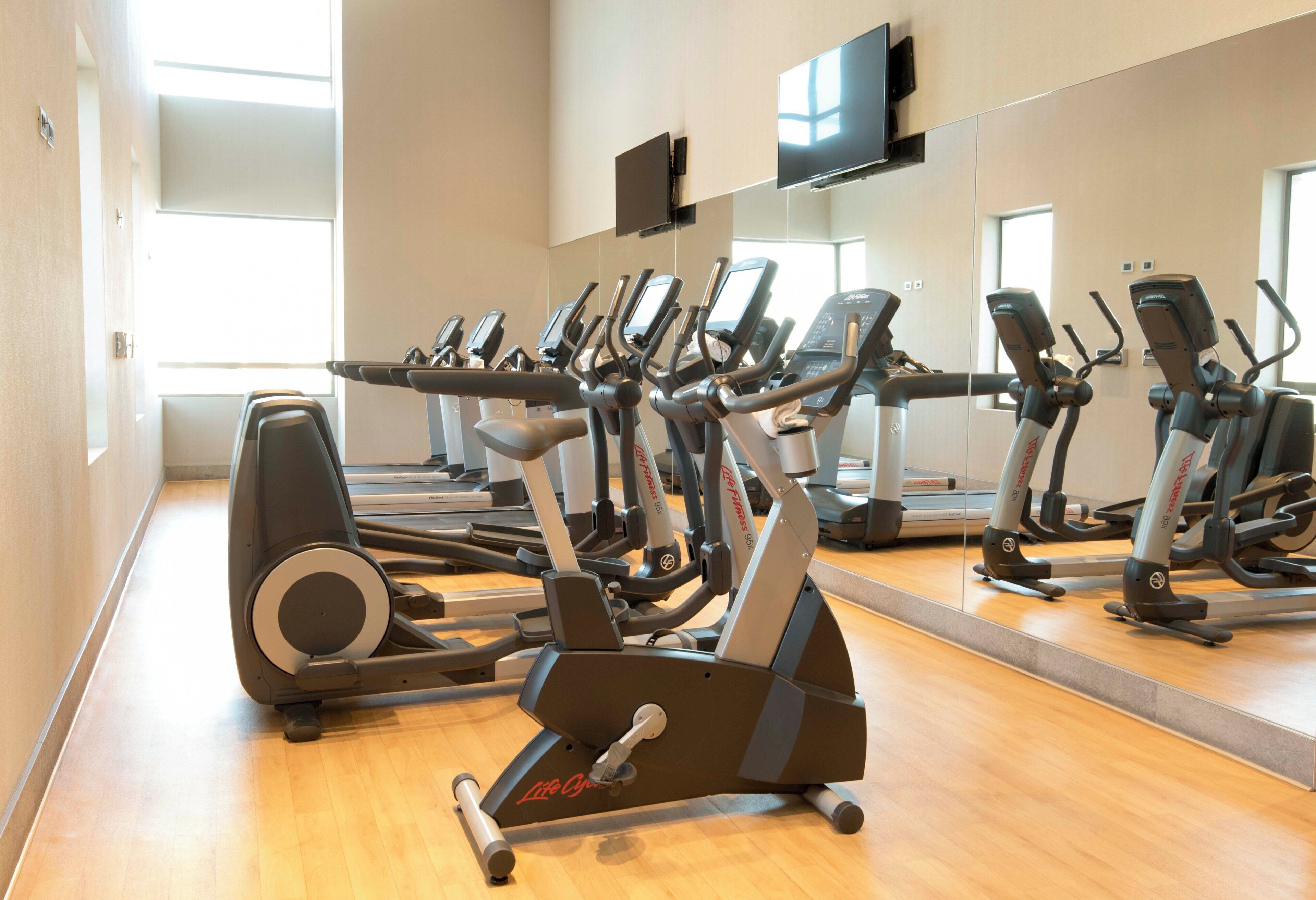 A gym with multiple cardio machines, including treadmills and elliptical trainers, arranged in rows.