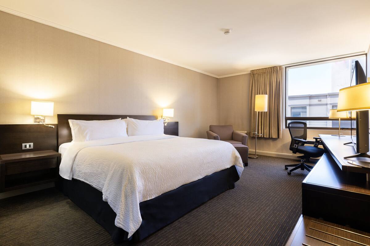 A hotel room with a large bed, a desk, a chair, and a window with curtains.