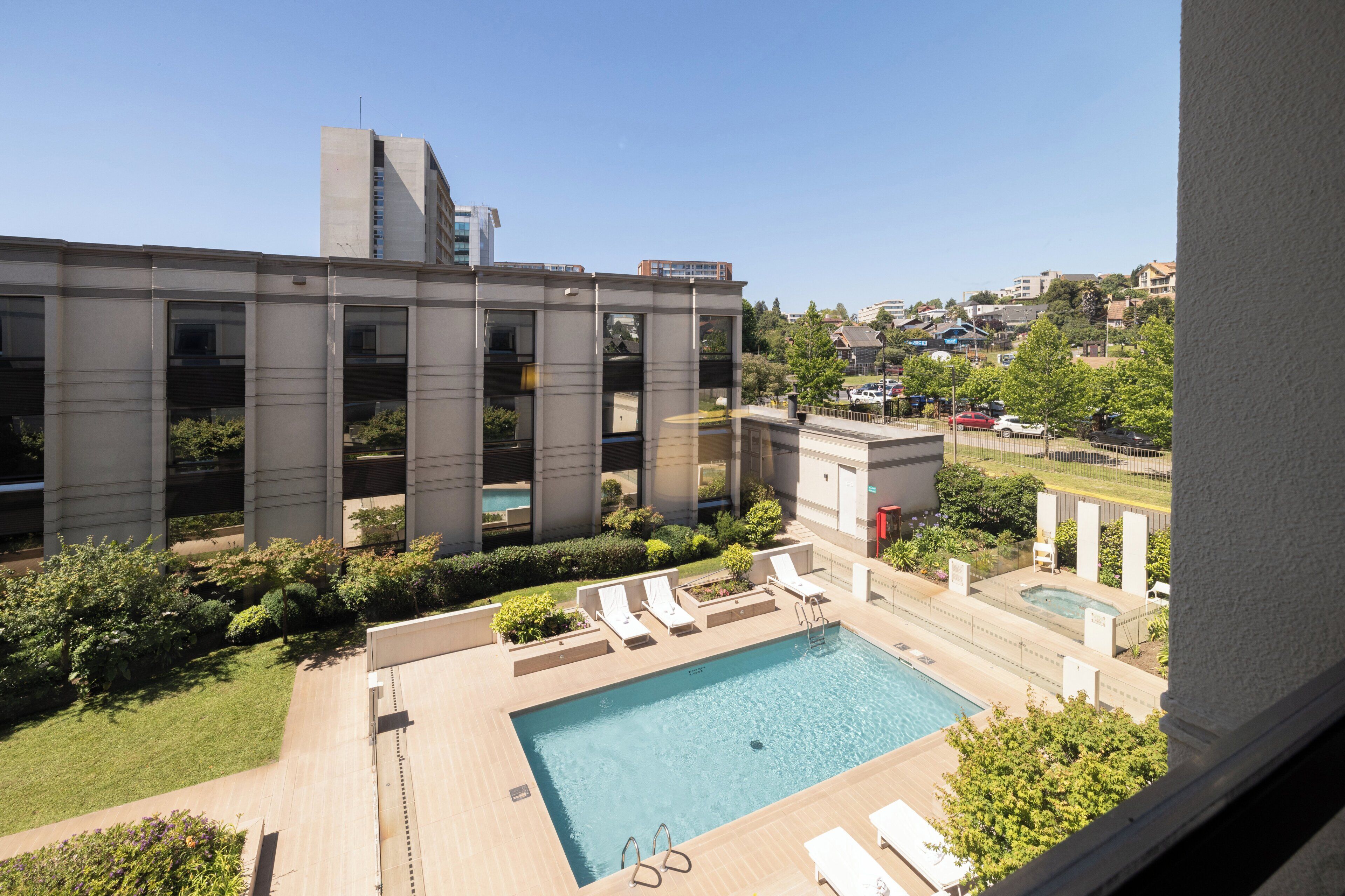 A modern building with a swimming pool and lounge chairs.