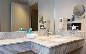 A hotel bathroom with a marble sink, a large mirror, a hairdryer, and a towel rack.