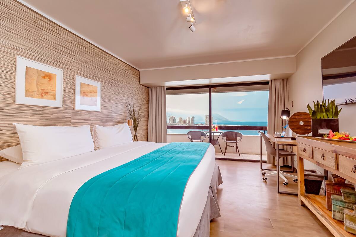 A modern hotel room with a large bed, a desk, and a view of the city.