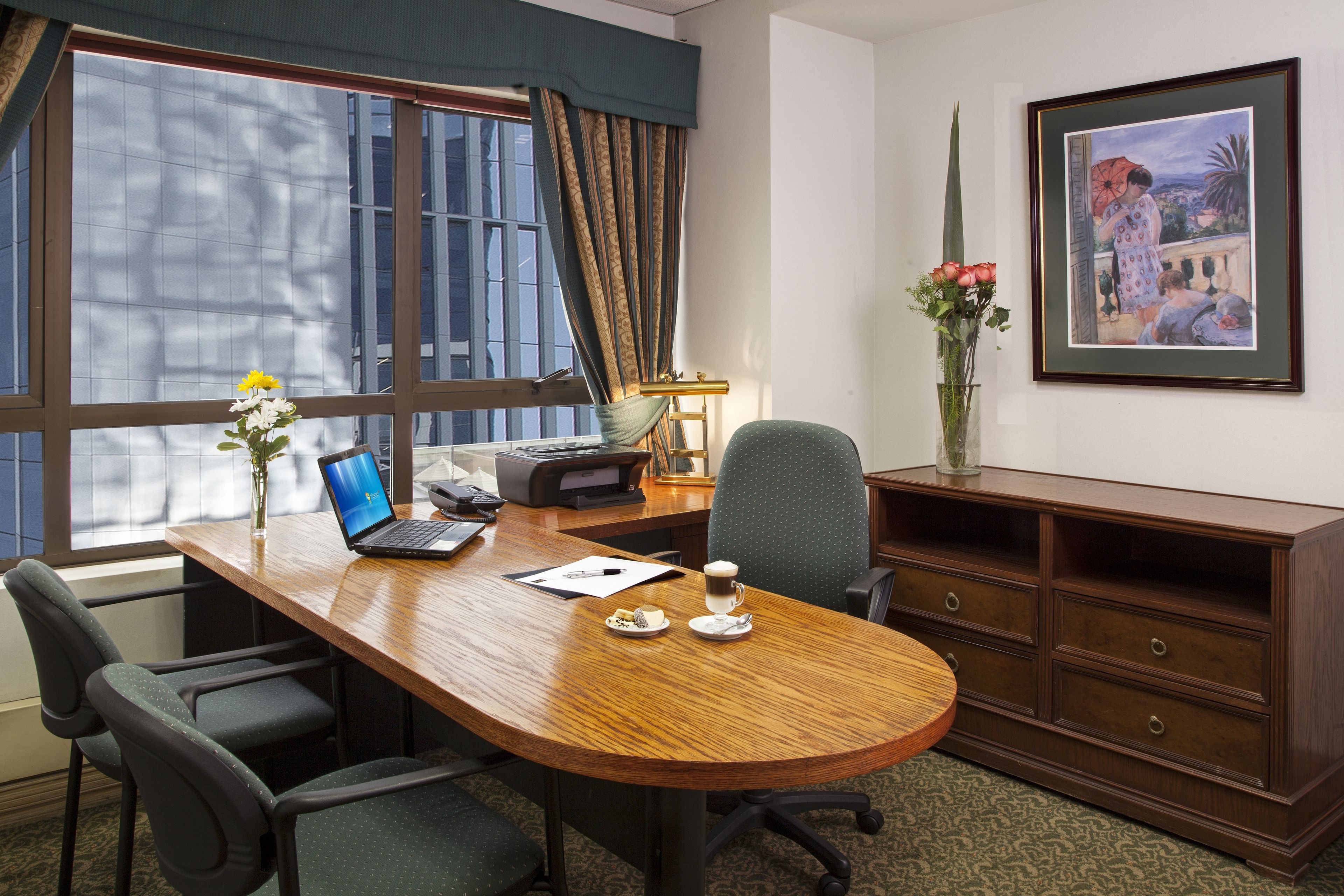 A conference room with a wooden table, chairs, a laptop, a coffee cup, and a framed painting on the wall.