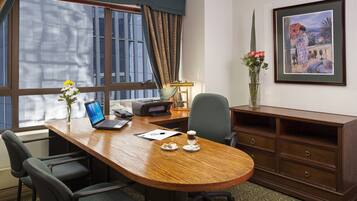 A conference room with a wooden table, chairs, a laptop, a coffee cup, and a framed painting on the wall.