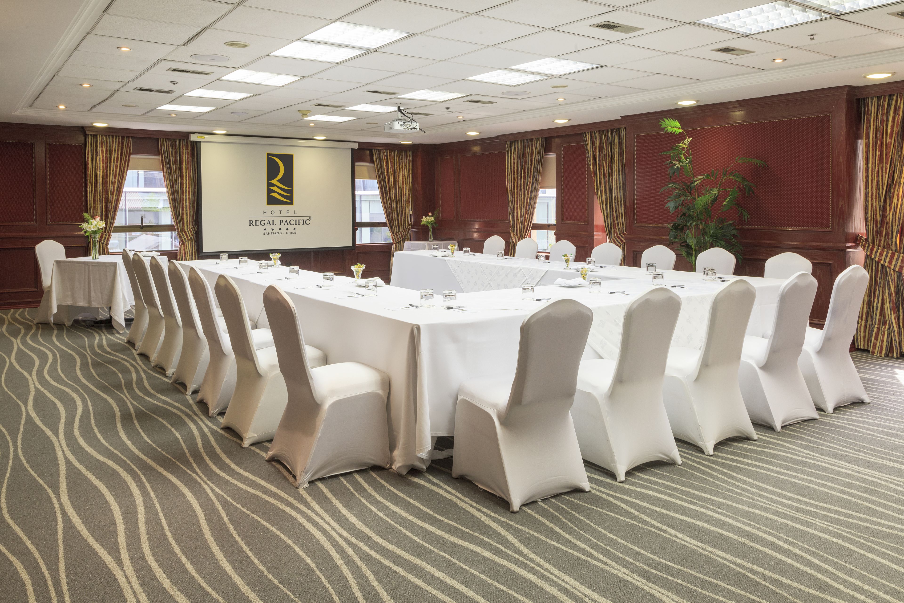 A conference room with a long table, white chairs, and a projector screen.
