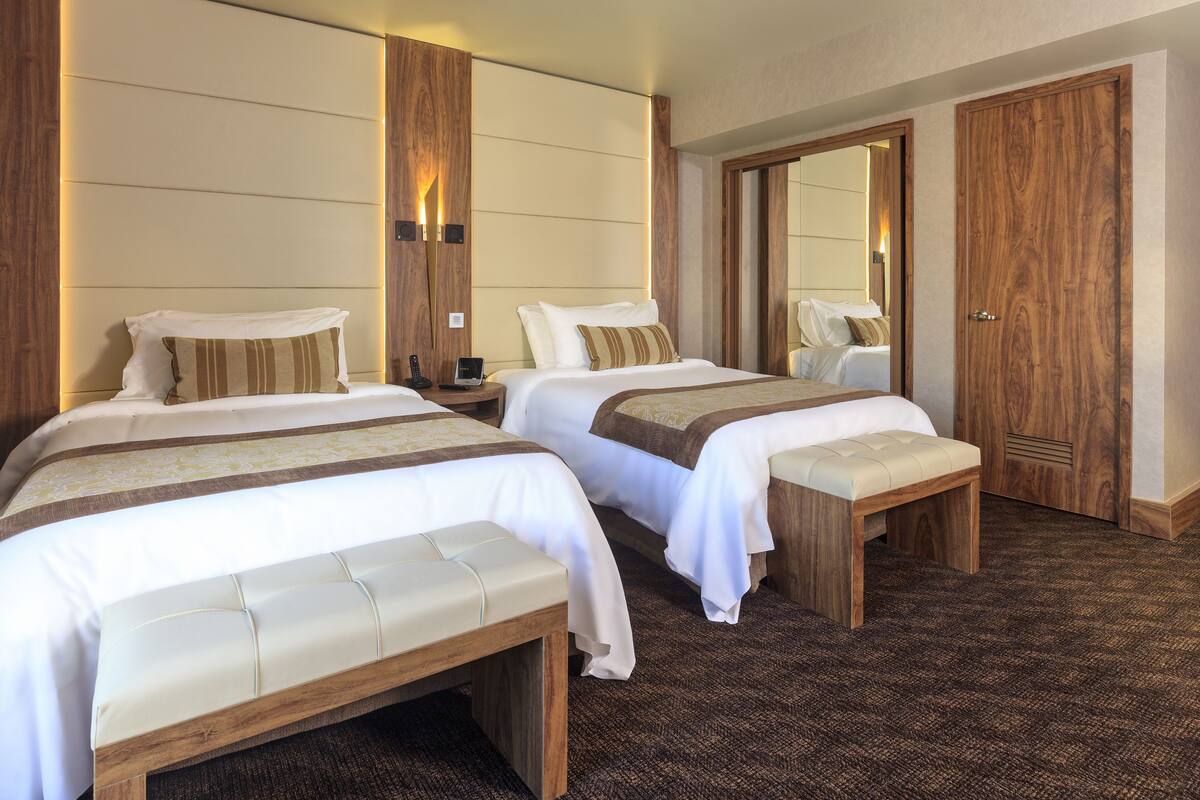 Een hotelkamer met twee bedden, houten hoofdborden, nachtkastjes en een grote spiegel.