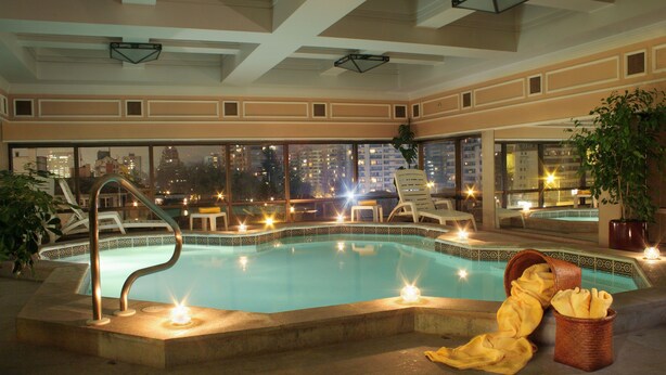 A swimming pool with a view of the city at night, surrounded by lounge chairs and a basket of bread. - Regal Pacific Hotel Santiago (Santiago)