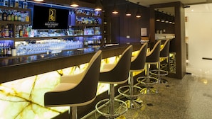 A bar area with a marble countertop, multiple liquor bottles, and black bar stools. - Regal Pacific Hotel Santiago (Santiago)