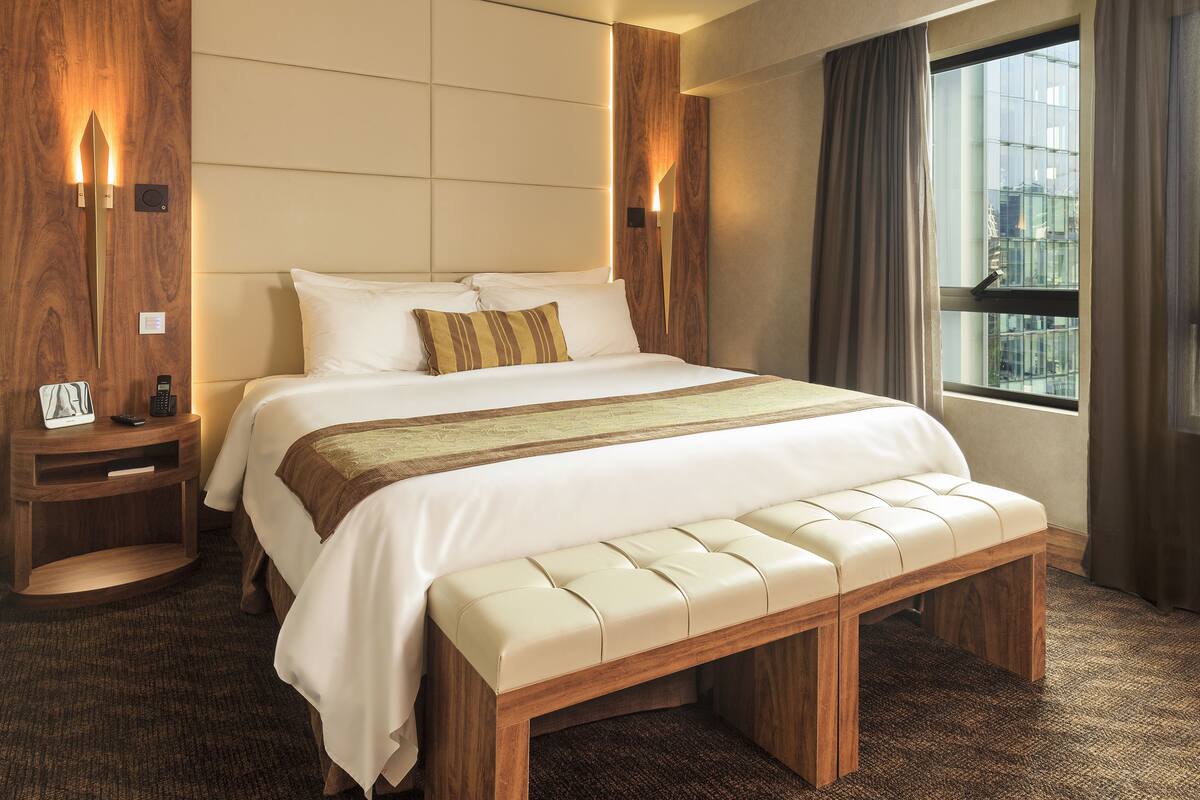 Een moderne hotelkamer met een groot bed, een houten hoofdeinde en een bank bij het voeteneinde.