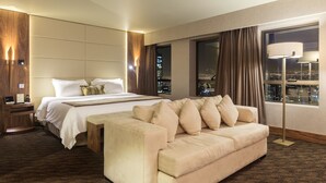 A hotel room with a large bed, a sofa, a nightstand, and a view of the city at night. - Regal Pacific Hotel Santiago (Santiago)