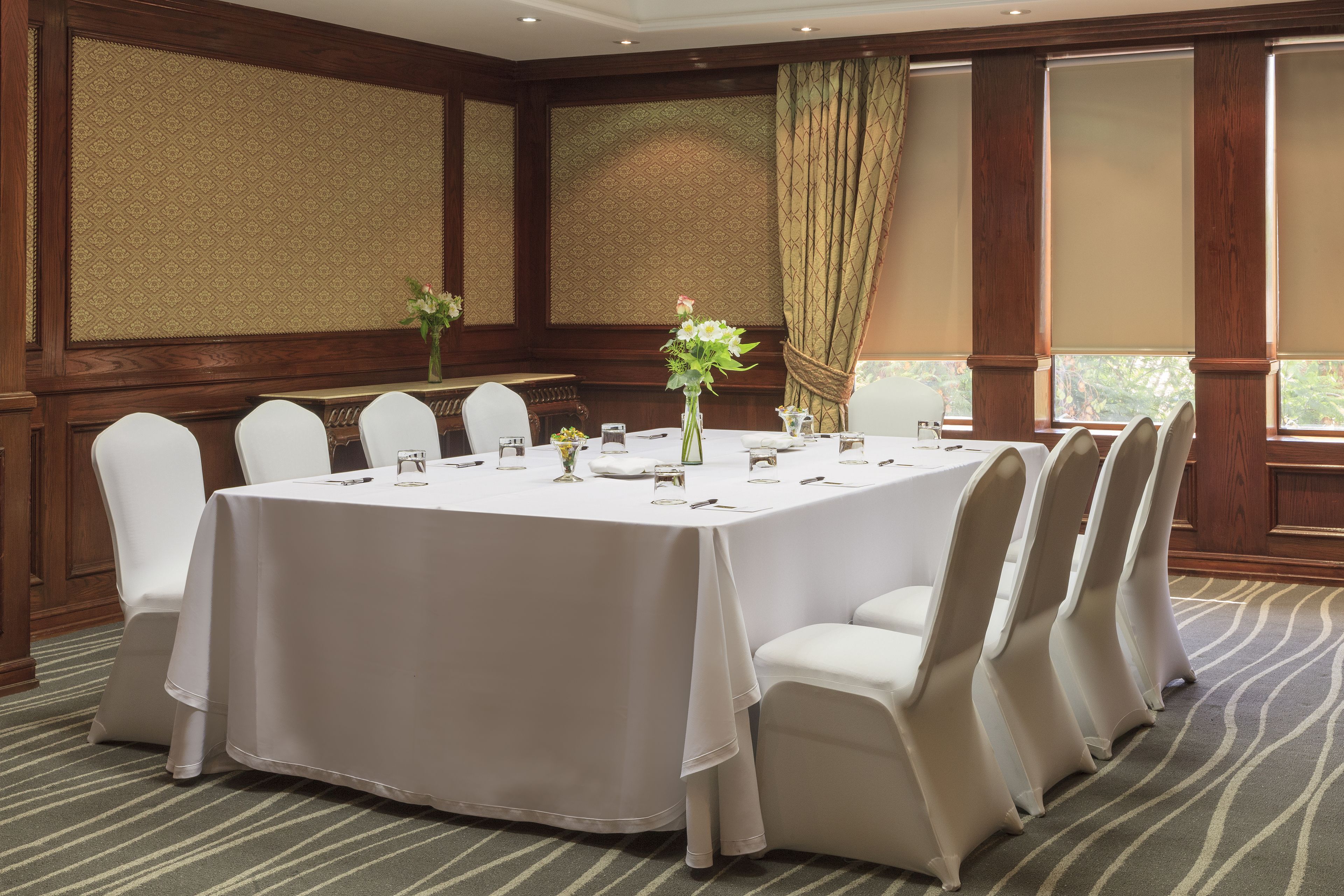 Une salle de conférence avec une table ronde, des chaises blanches et un arrangement floral au centre.