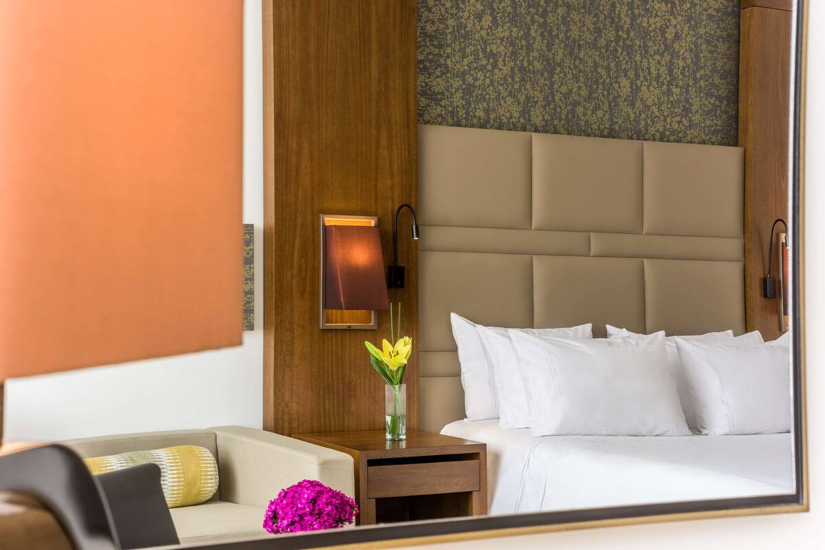 A hotel room with a bed, a nightstand, a lamp, and a vase with flowers.