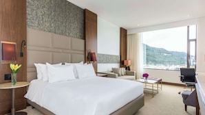 Habitación de hotel con una cama grande, un escritorio, una silla, una mesita de noche y vistas a un paisaje montañoso.