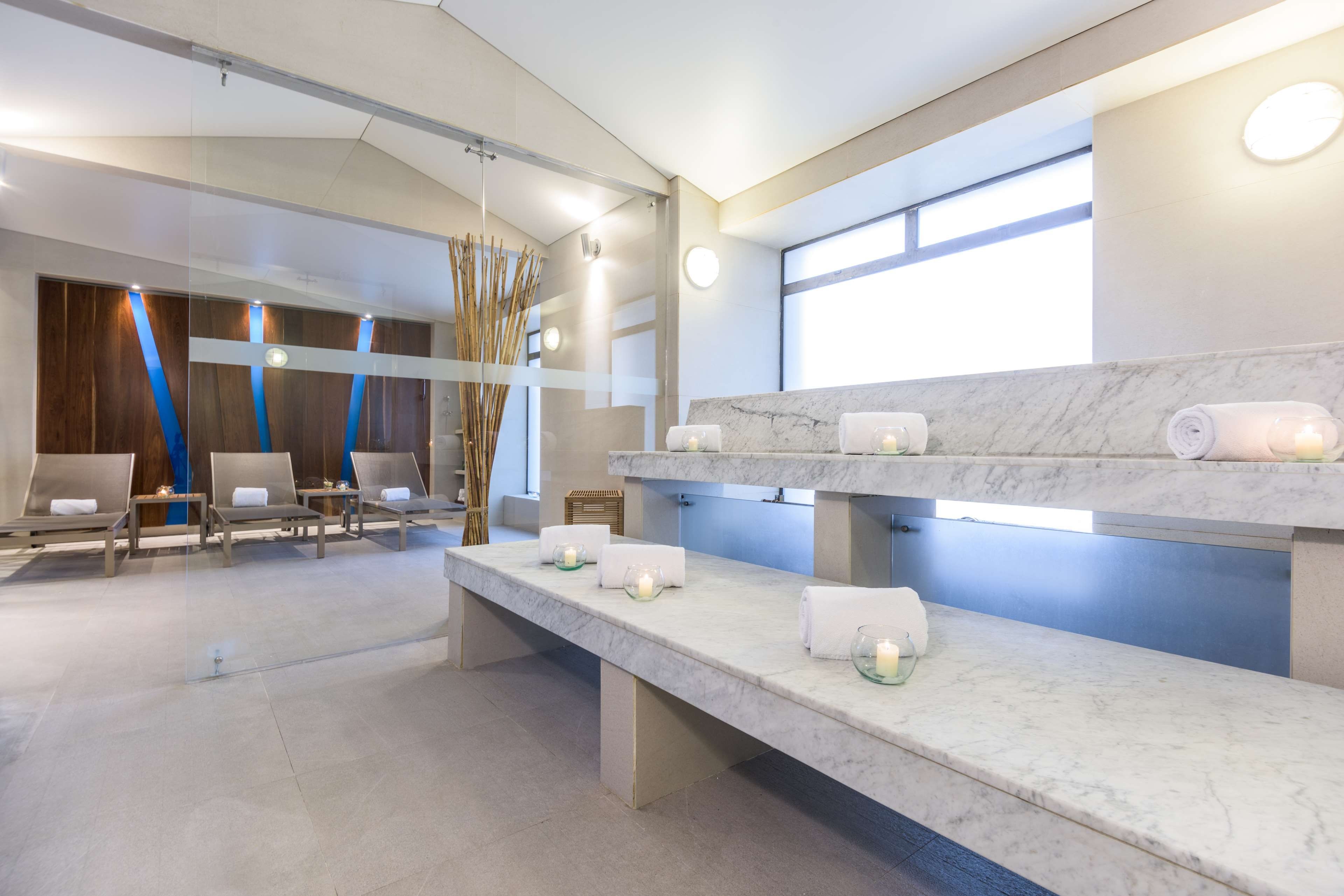 Un moderno espacio de spa con mostrador de recepción, zona de estar y una barra de mármol con toallas y velas.