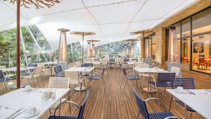 An outdoor dining area with wooden flooring, white tables, and blue chairs. - NH Collection Bogotá Teleport Royal (Bogotá)