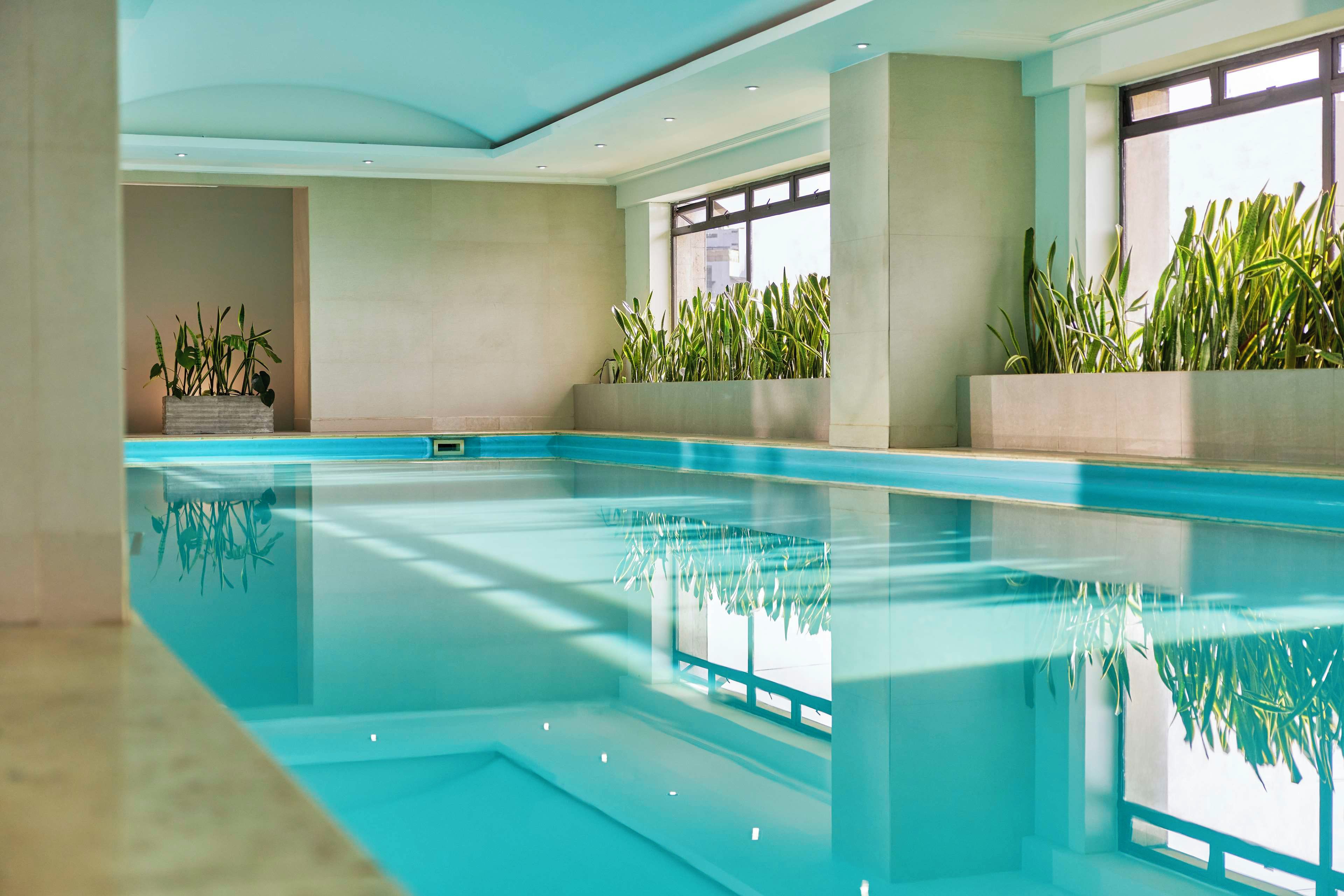An indoor swimming pool with clear water, surrounded by walls and windows.