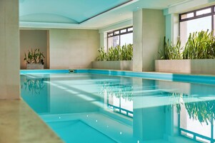 Una piscina interna con acqua cristallina, circondata da pareti e finestre.