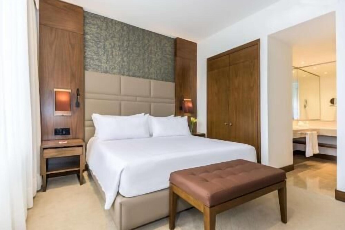 A hotel room with a bed, a wooden bench, a nightstand, a wardrobe, and a mirror.