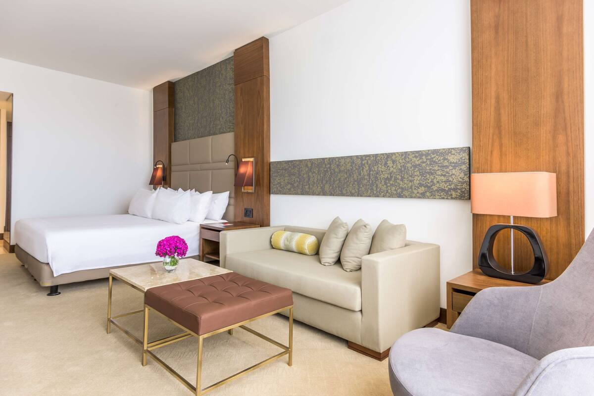 A hotel room with a bed, a sofa, a coffee table, and a lamp.