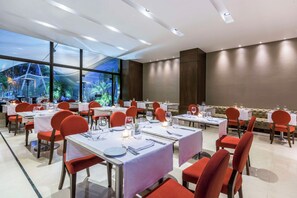 A restaurant with tables set for dining, red chairs, and a view of greenery through large windows. - NH Collection Bogotá Teleport Royal (Bogotá)