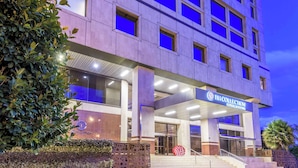 Fachada de hotel con diseño moderno, destacada por un letrero llamativo y una escalera que conduce al vestíbulo.