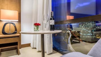Habitación de hotel con una mesa redonda, una botella de vino, una copa y un jarrón con flores.