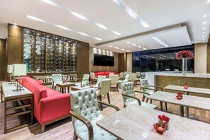 A modern hotel lobby with seating areas, a wine display, and a large TV screen. - NH Collection Bogotá Teleport Royal (Bogotá)
