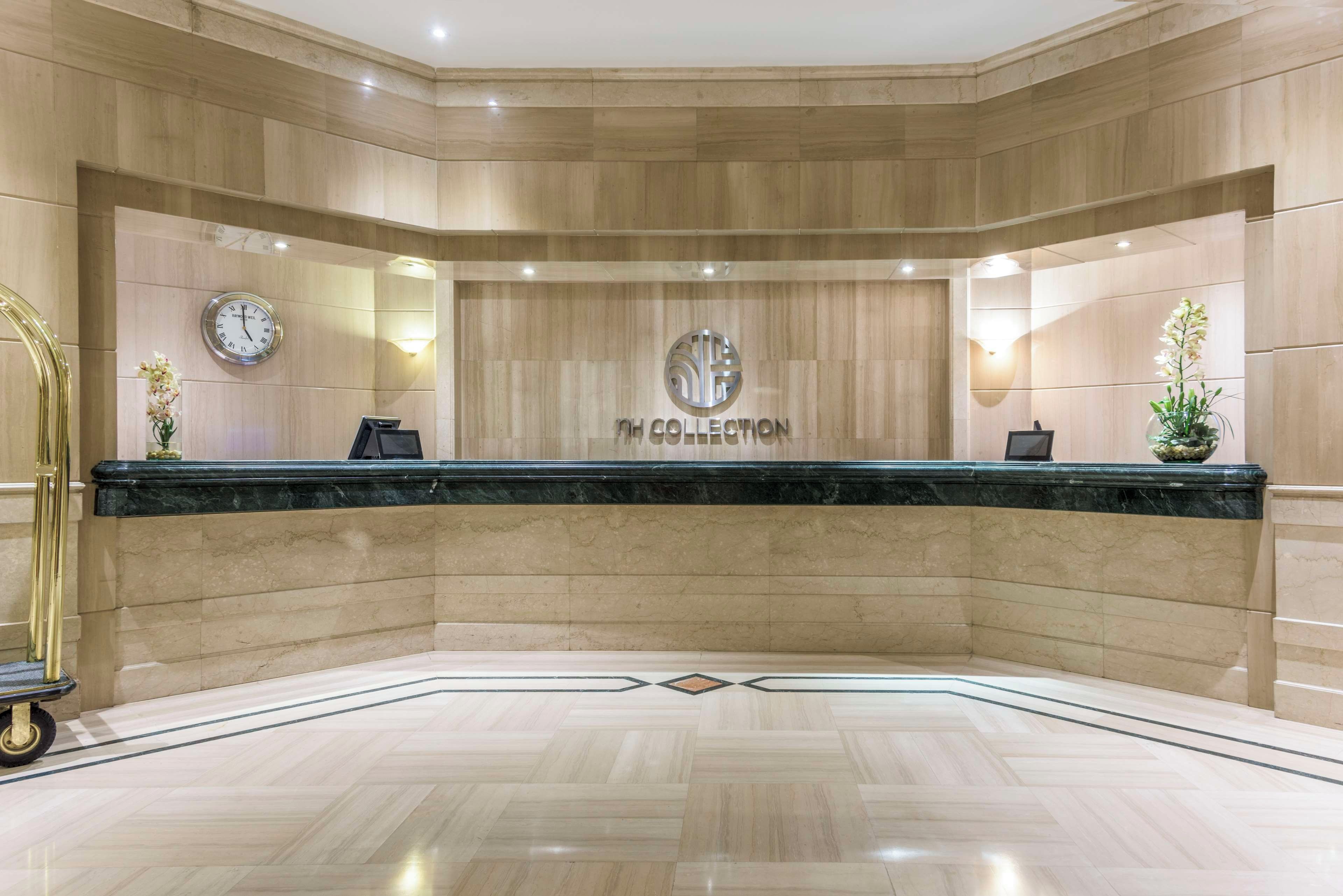 Zona de recepción con mostrador de mármol, un reloj y el logotipo de NH COLLECTION.