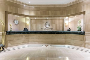Zona de recepción con mostrador de mármol, un reloj y el logotipo de NH COLLECTION.