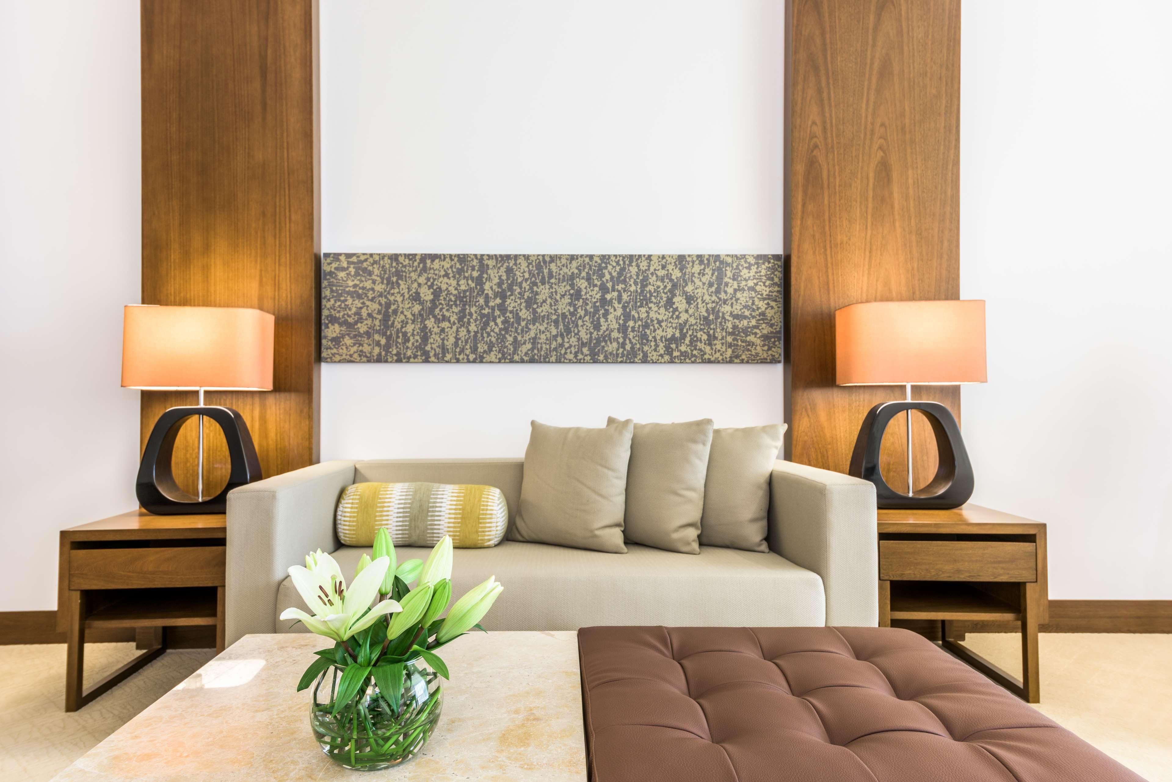 A modern living room with a sofa, two side tables with lamps, a coffee table, and a decorative vase with flowers.