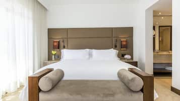 A modern hotel room with a large bed, a wooden headboard, a bedside table with a lamp, and a view of the bathroom.