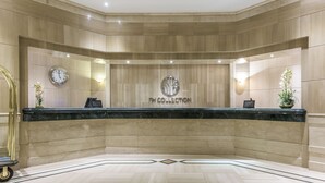 A reception area with a marble counter, a clock, and a logo on the wall. - NH Collection Bogotá Teleport Royal (Bogotá)