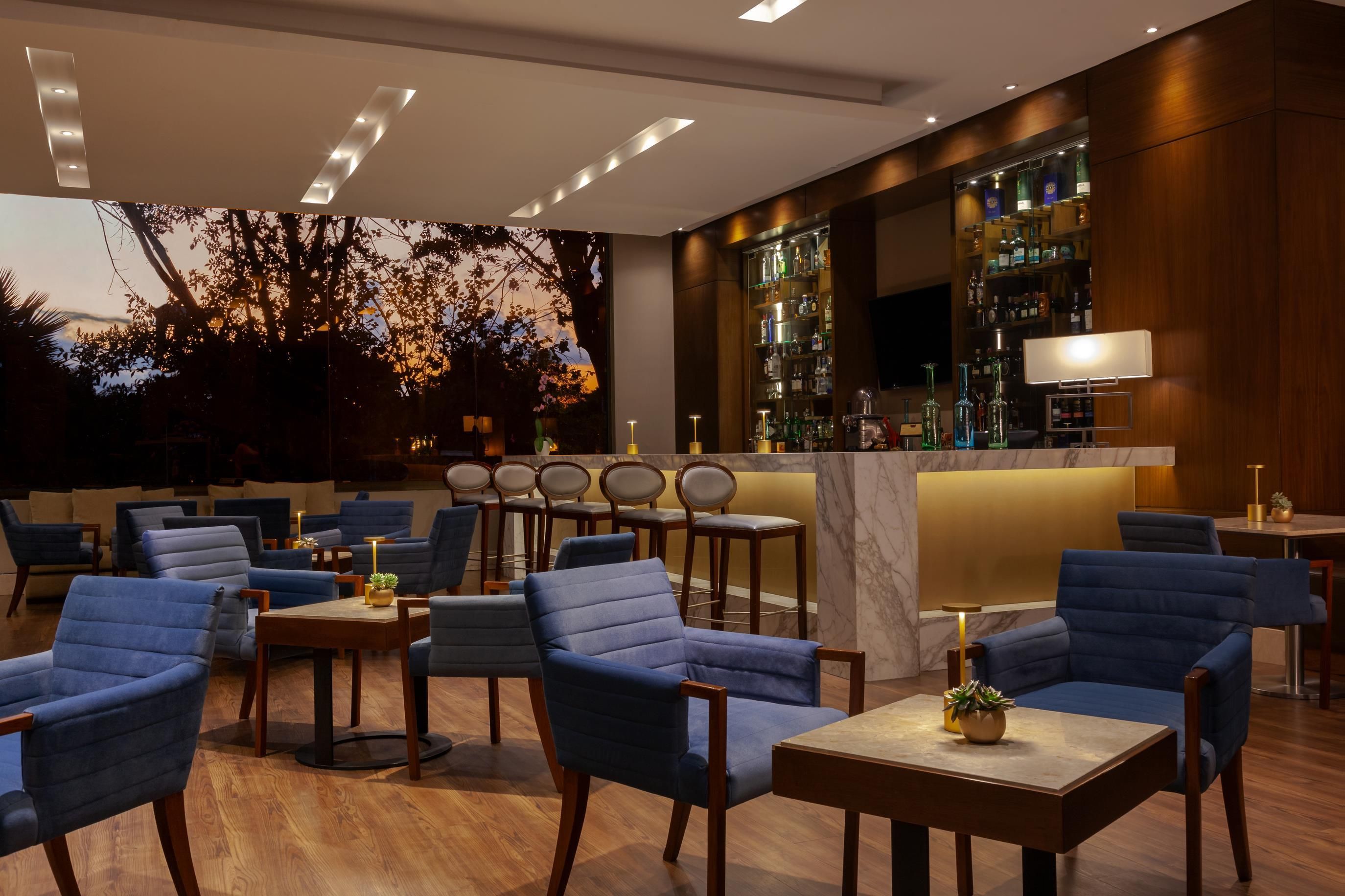 A modern bar area with blue upholstered chairs, wooden tables, and a bar stocked with bottles.
