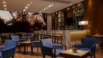 Un área de bar moderna con sillas tapizadas en azul, mesas de madera y una barra repleta de botellas.