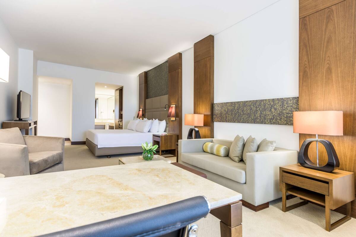 A modern hotel room with a bed, a sofa, a desk, and a TV.