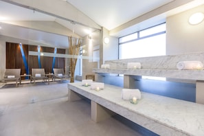 Relax in a serene spa area with cushioned seating, a marble reception desk, and a large window.