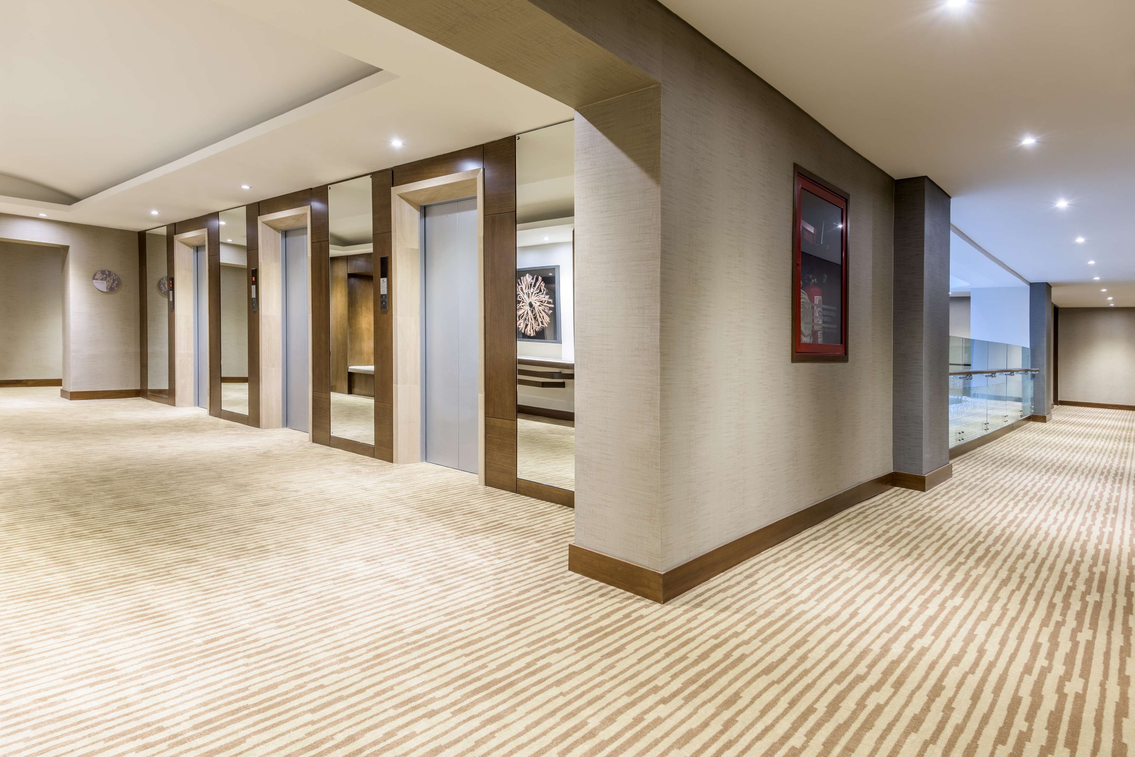 A hotel corridor with a carpeted floor, wooden paneling, and a glass railing on the right.