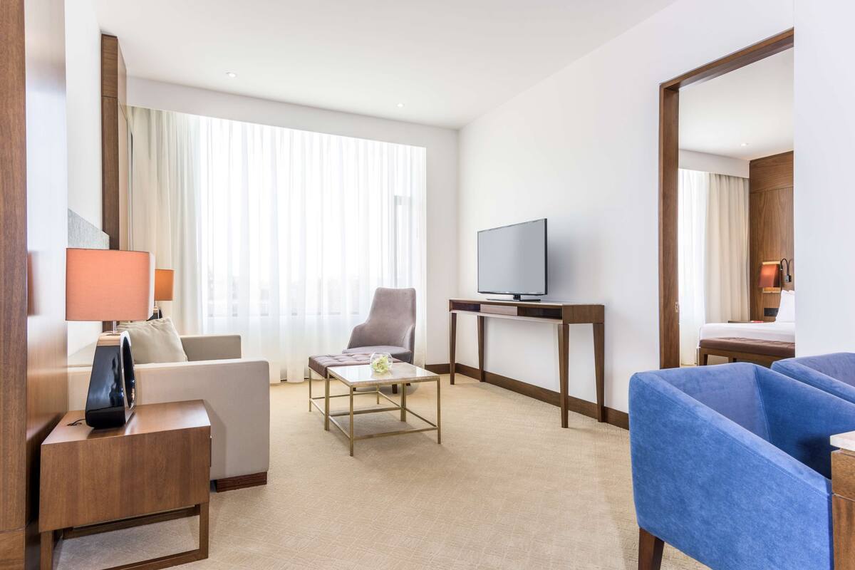 A hotel room with a sofa, a chair, a coffee table, a TV on a stand, and a bed.