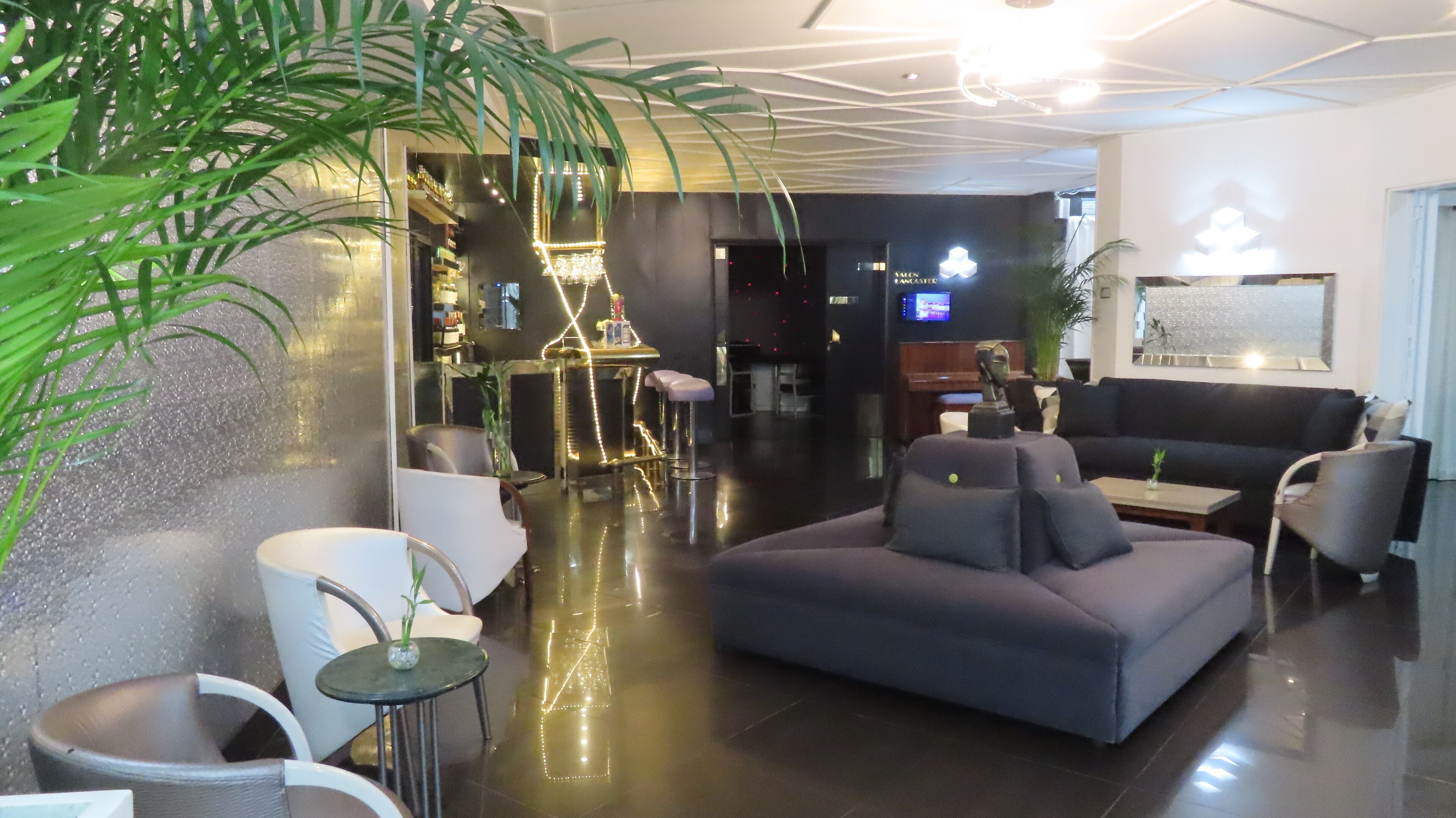 A modern lobby with a grey sofa, white chairs, a small round table, and a bar area with stools.