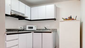 A compact kitchen with white cabinets, a microwave, a sink, and a refrigerator.