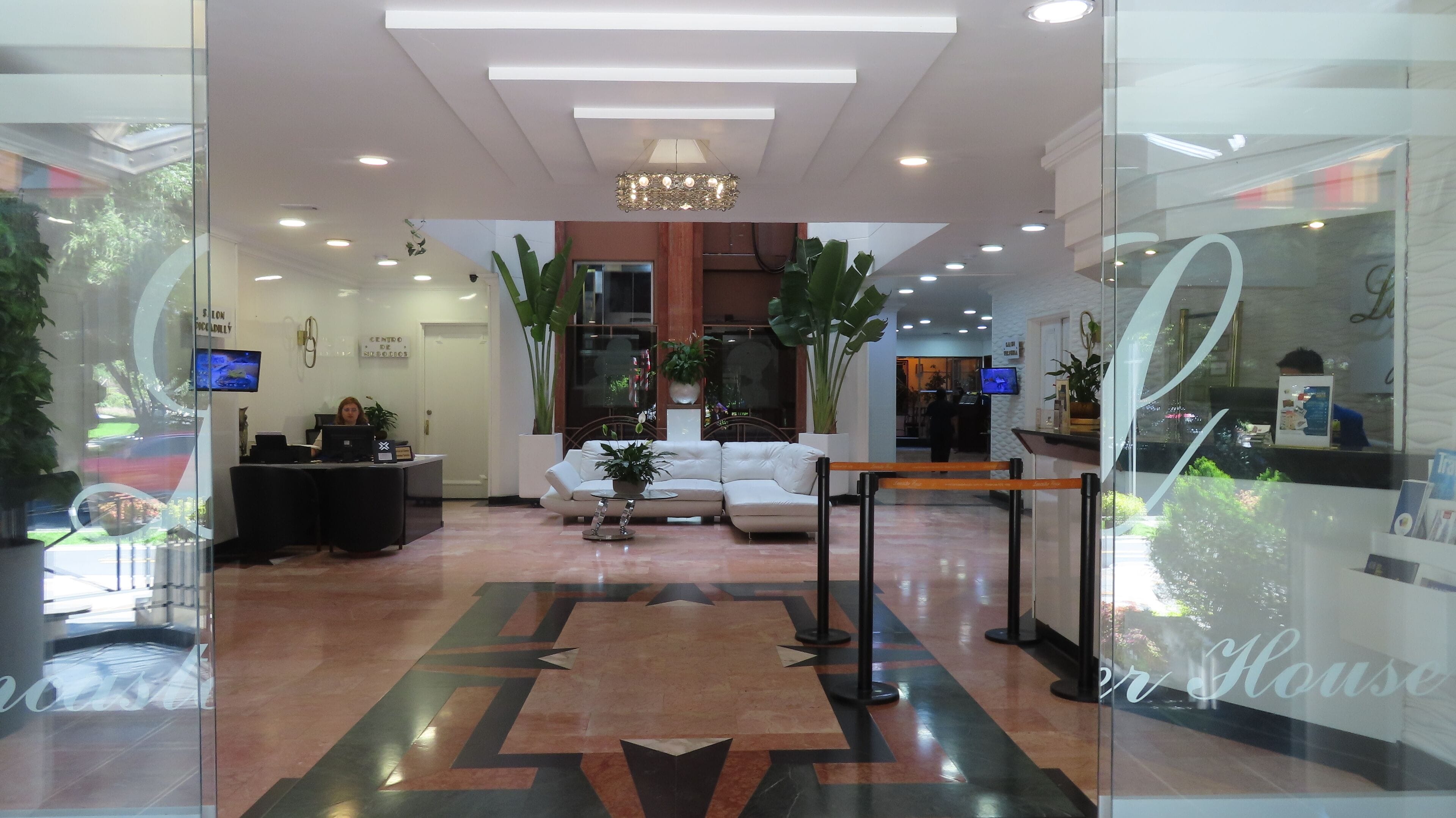 A modern hotel lobby with a reception desk, seating area, and a large chandelier.