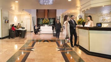 Un vestíbulo de hotel con mostrador de recepción, zona de estar y una gran lámpara de araña.