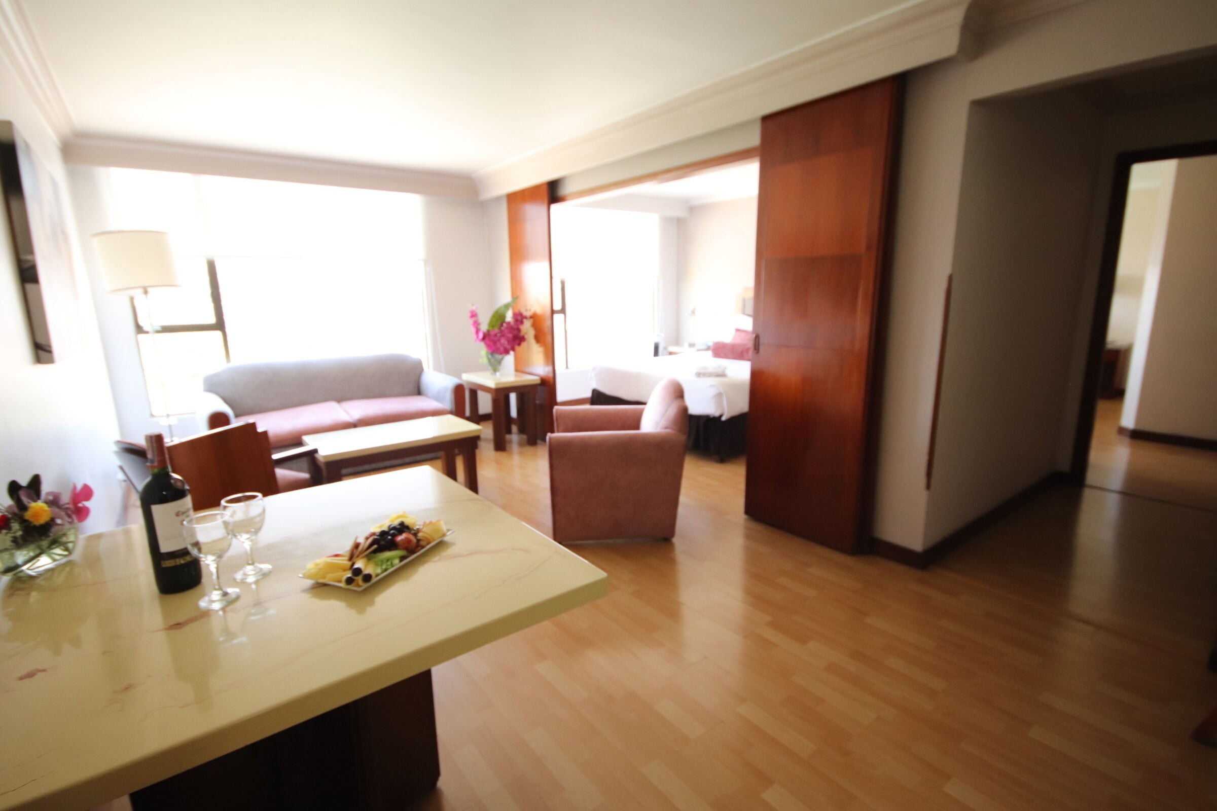 A modern living room with a wooden floor, a sofa, a coffee table, and a dining area with a table set for two.