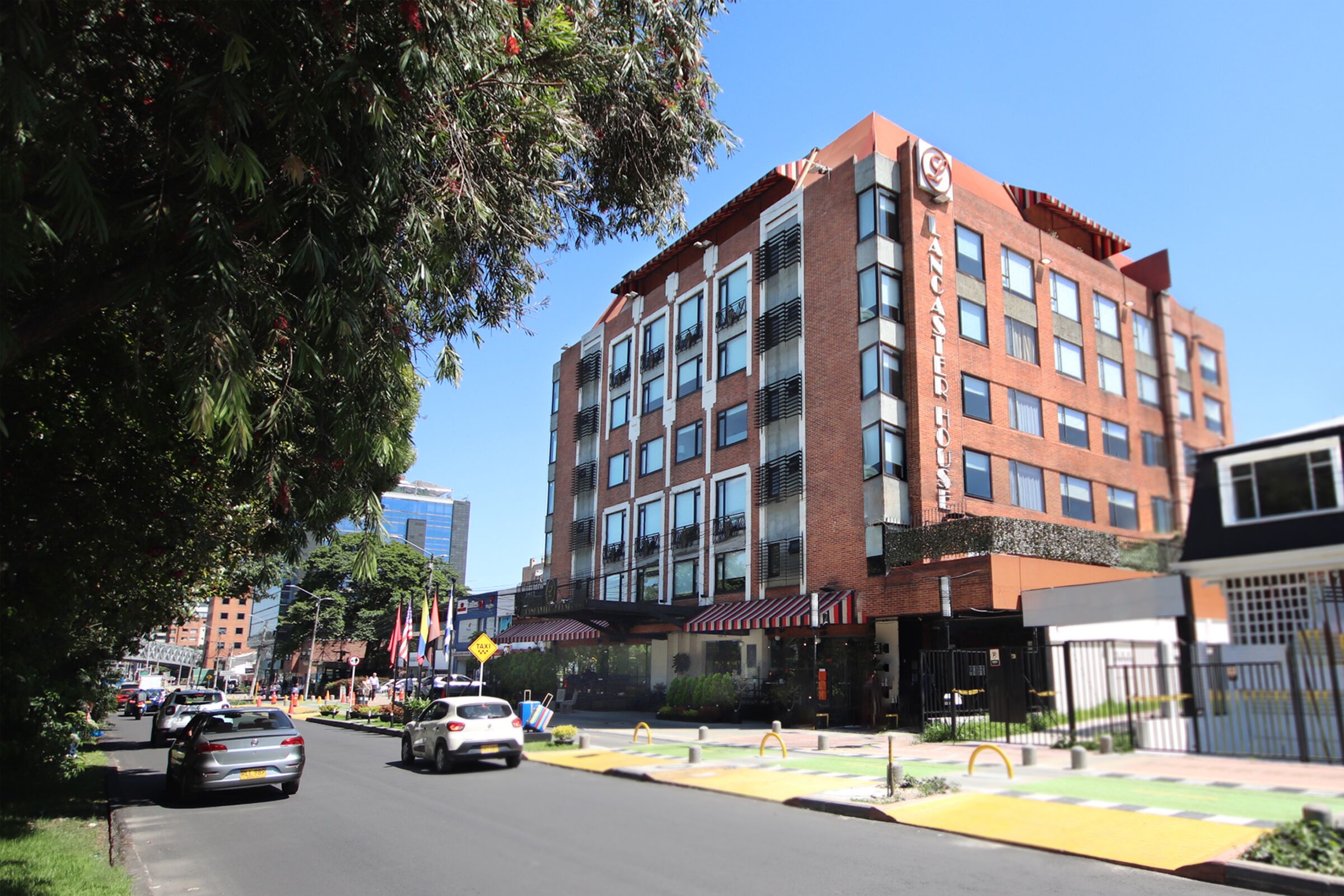 Un hotel de varios pisos con fachada de ladrillo rojo, ventanas grandes y una entrada visible con toldo rojo.