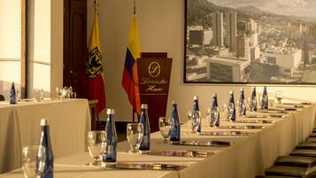 Un salón de conferencias con una larga mesa lista para una reunión, banderas y vistas panorámicas de la ciudad.