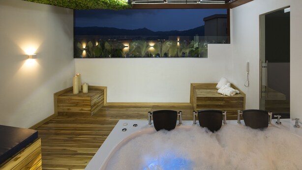 Een wellnessruimte met een jacuzzi, houten zitplaatsen en uitzicht op bergen in de nacht.